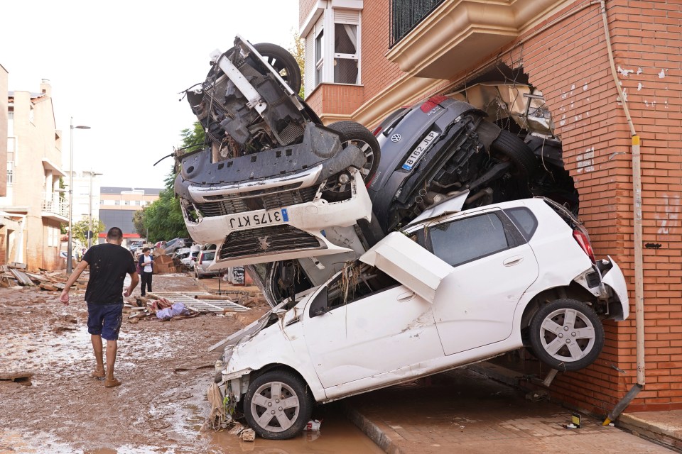 A man walks by piled up cars after floods in Massanassa, just outside of Valencia