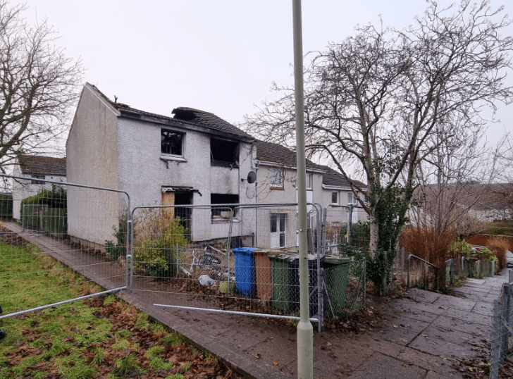 Fire-damaged house behind a fence.