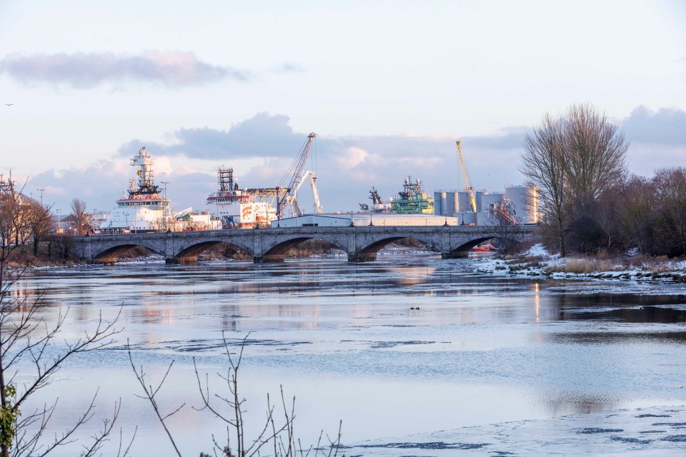 Victoria Bridge in Aberdeen, Scotland, with a partially frozen river and industrial area in the background.