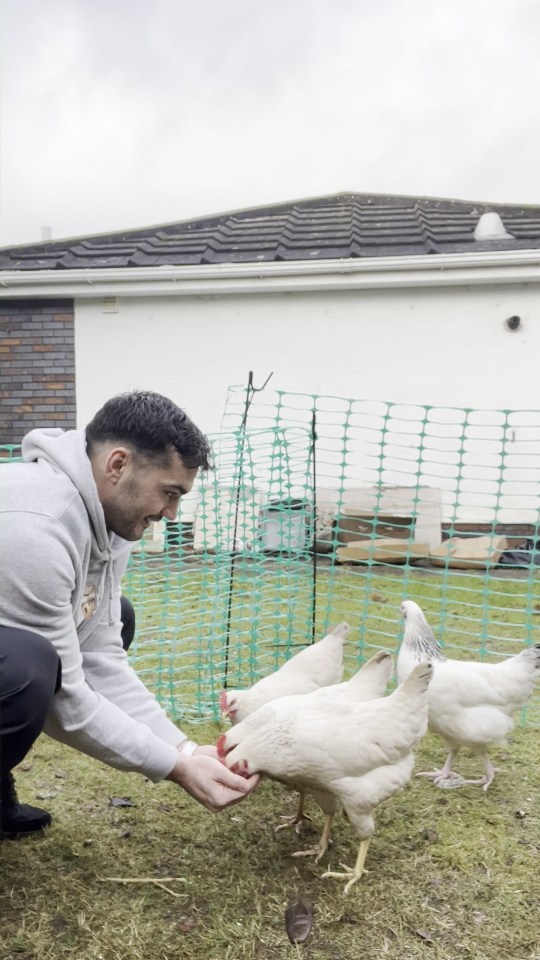 Man feeding chickens in a backyard coop.