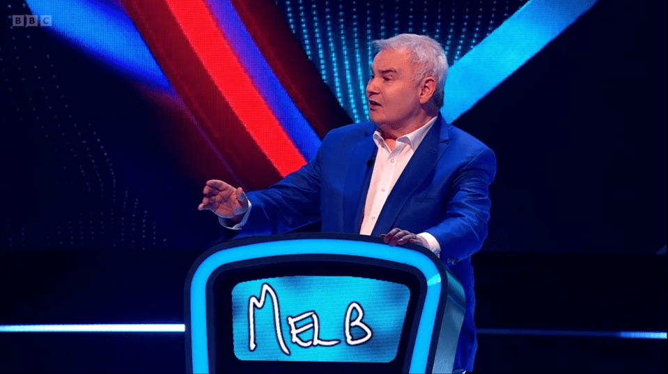 Screenshot of a man in a blue suit speaking at a game show podium.